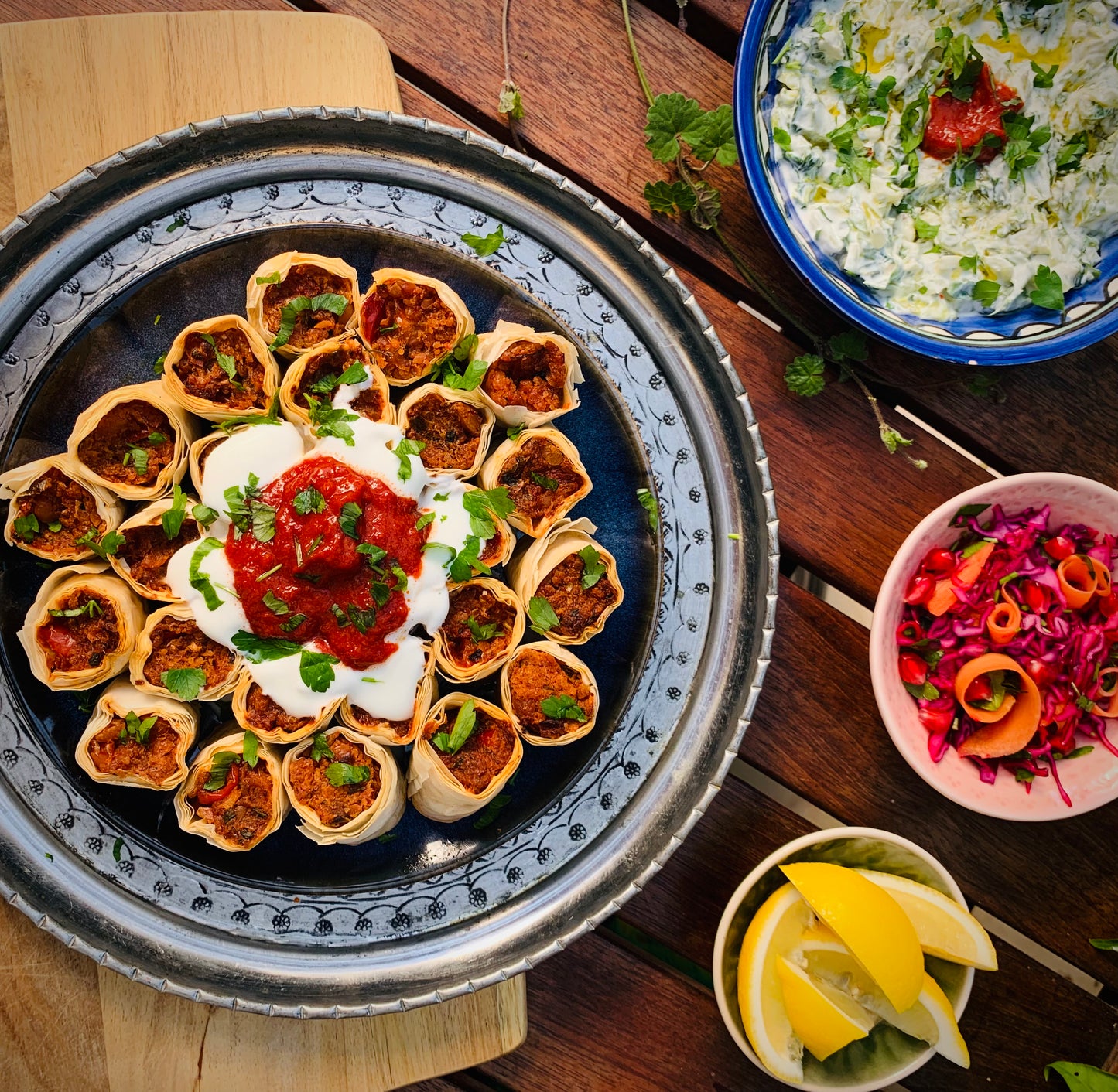 Experience bold vegetarian flavours with Event’s Mastering Bold Vegetarian Flavours—a tray of rolled pastries topped with yogurt and red sauce, served with tzatziki, red cabbage salad, and lemon wedges for an authentic Turkish feast.