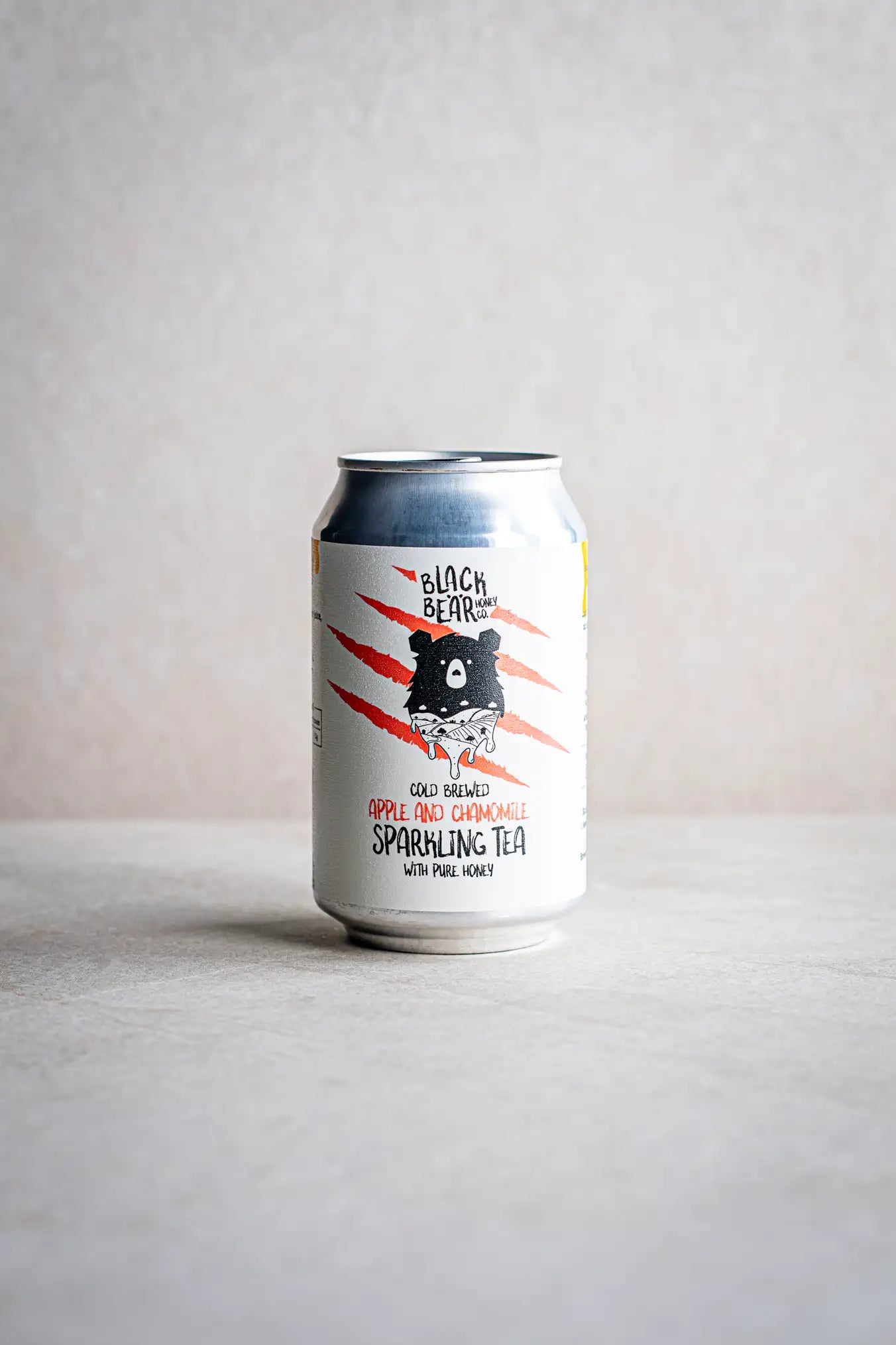 A can of Honesty Cold Brewed Sparkling Tea with Pure Honey, featuring a crisp silver can with a white label, a bear illustration, and bold red claw marks on a light background for a refreshing look.