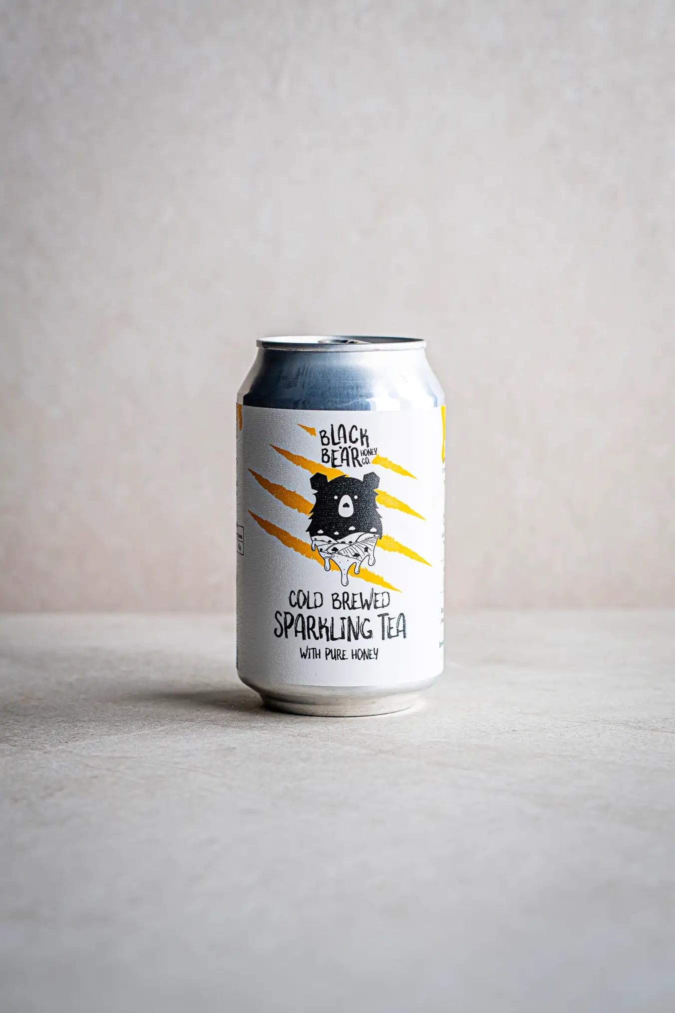 A can of Honesty Cold Brewed Sparkling Tea with Pure Honey rests on a light surface against a neutral background, its label displaying an illustrated bear and bold yellow claw marks.