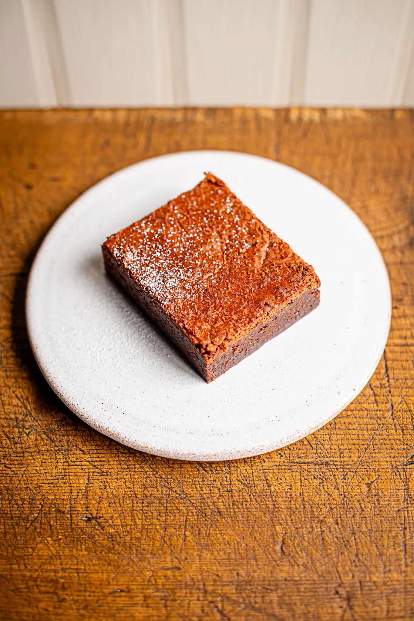 A single Honesty chocolate brownie sits on a round white plate, placed on a wooden surface.