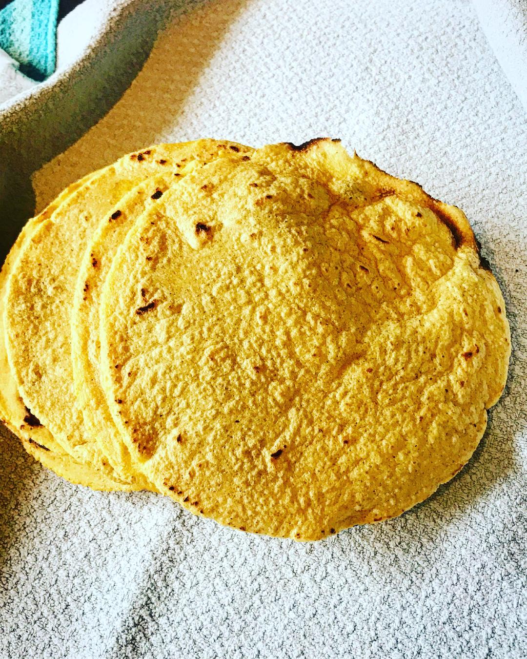 Three golden corn tortillas from Events Mexican Street Food are stacked on a light, textured surface, highlighting their slightly rough texture and distinctive edges.
