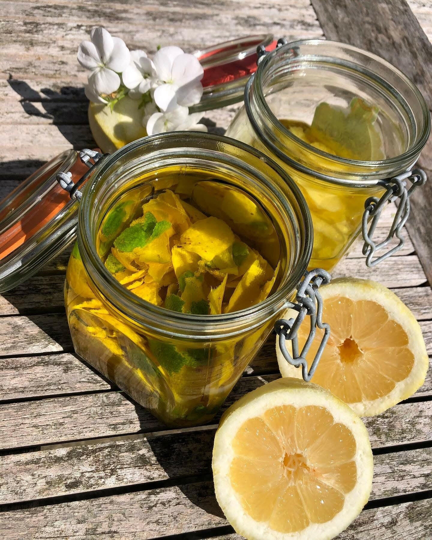 Two glass jars of Events Edible Christmas Gifts...Buon Natale, as they say in Italy sit on a rustic wooden table beside a halved lemon and a white flower in a vase, bathed in soft sunlight.