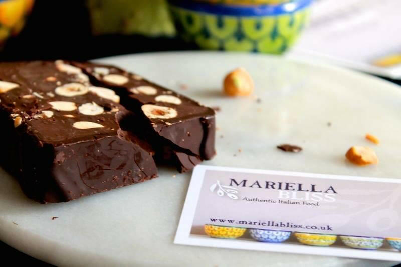 Two pieces of chocolate with whole hazelnuts sit on a white plate beside an Event business card. Nearby are some loose hazelnuts and a slice of Panforte di Siena from the Edible Christmas Gifts...Buon Natale, as they say in Italy collection.