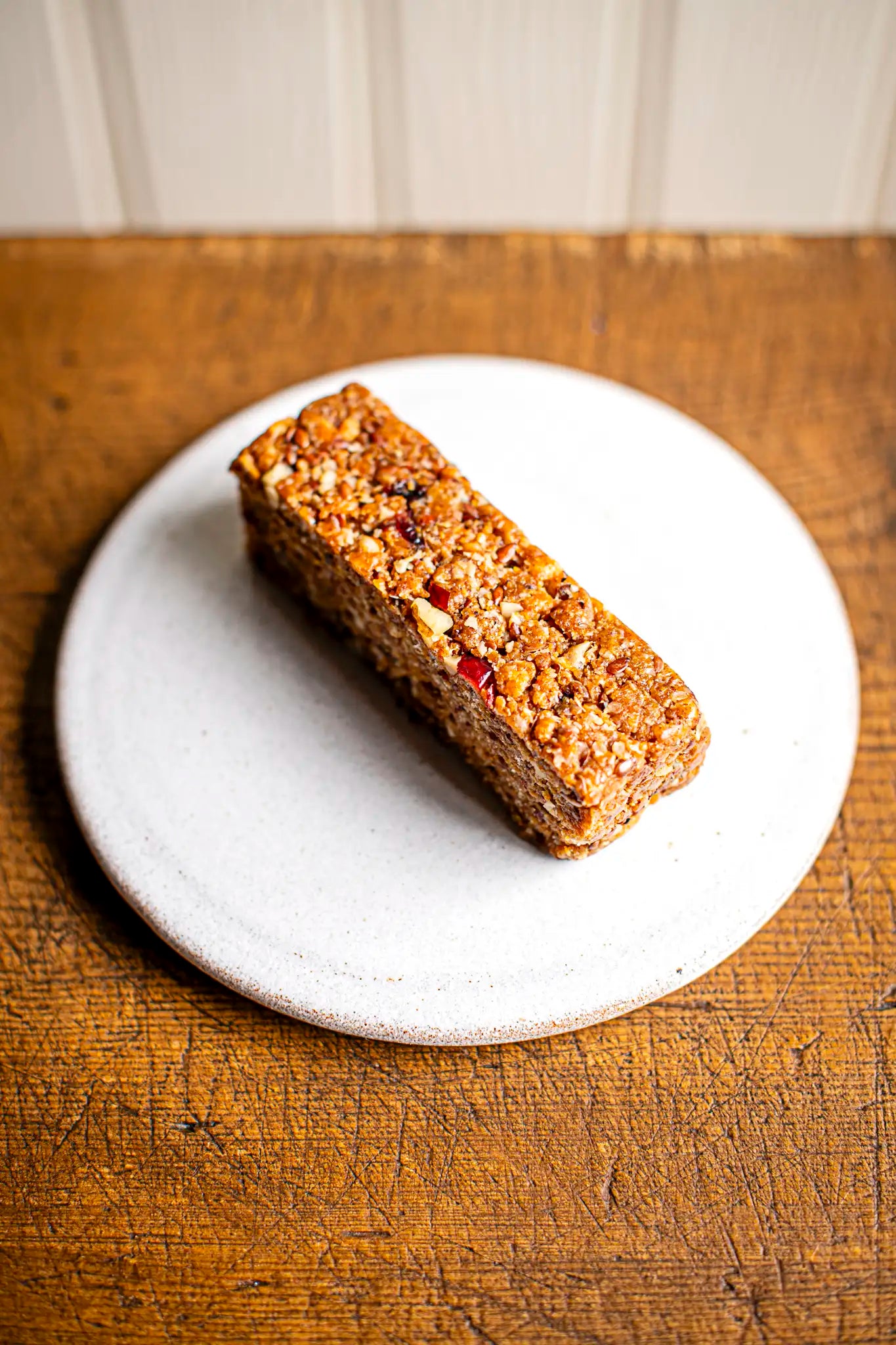 A Honesty Victoria Sponge sits on a white plate atop a wooden surface.
