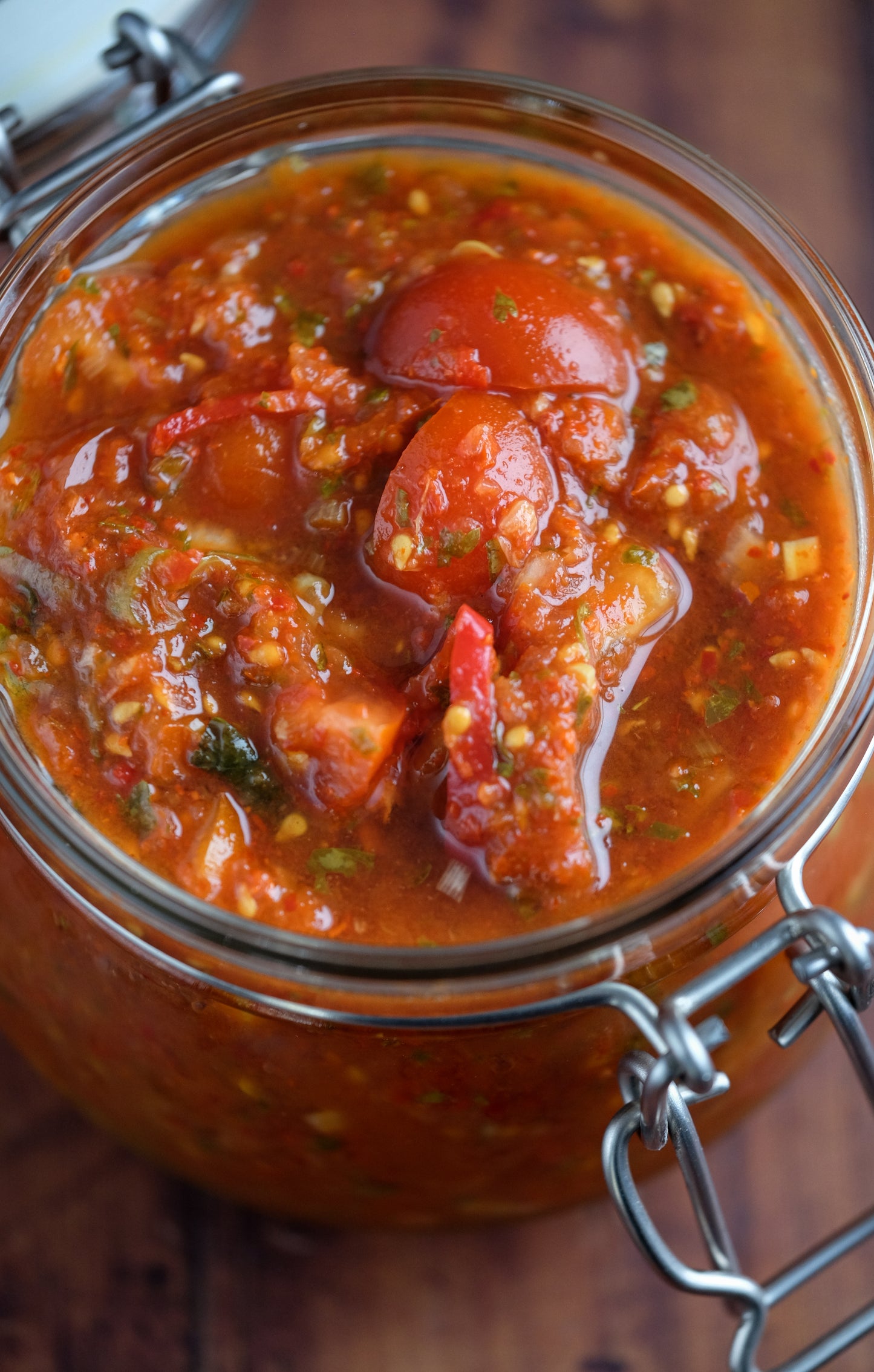 A close-up of a glass jar filled with chunky red salsa, highlighting tomato, herbs, and spices. Ideal for fans of the Fermented Foods Workshop by Event and those interested in gut health. The open jar rests on a wooden surface.