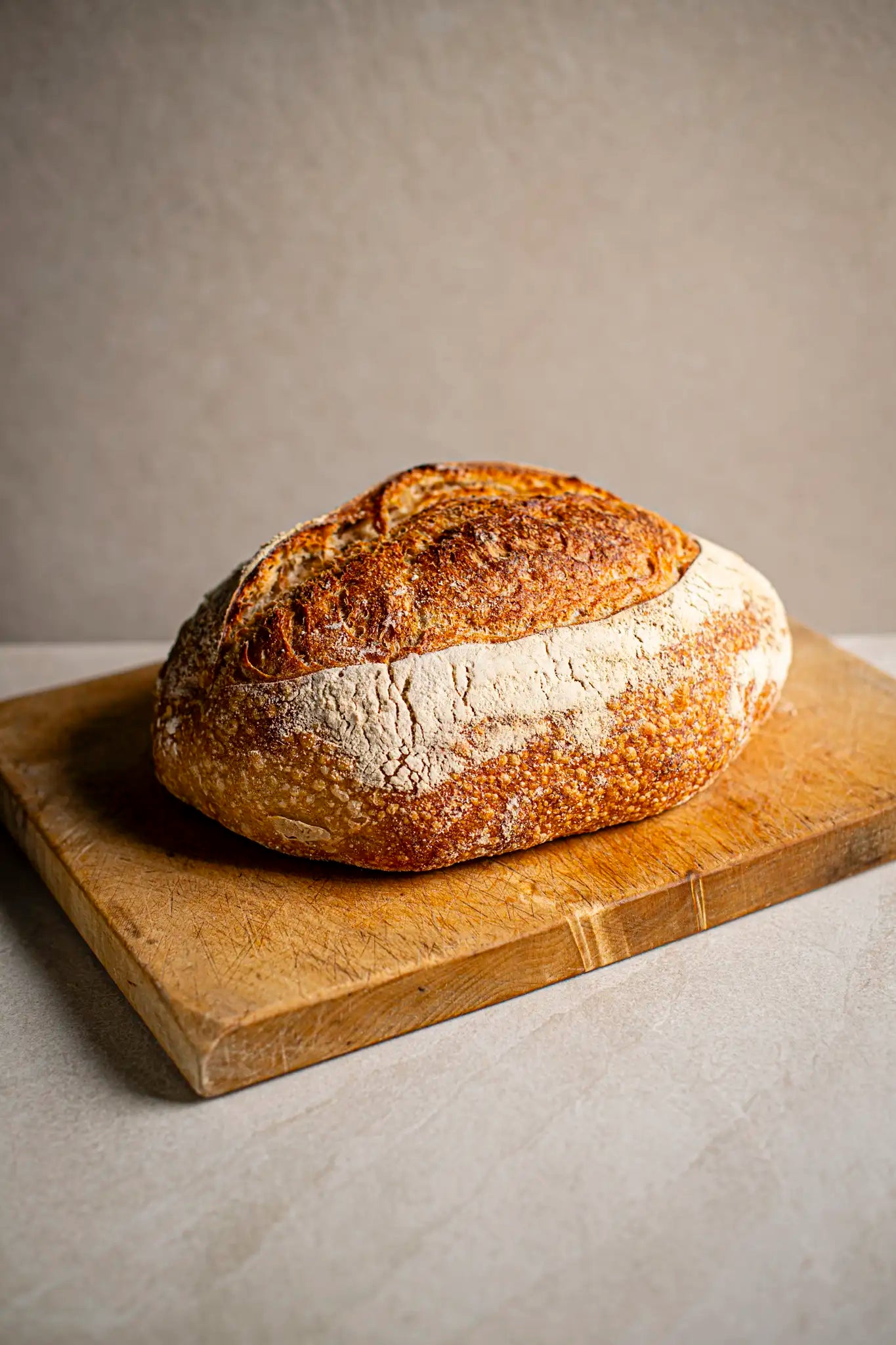 A classic Sourdough by Honesty sits on a wooden cutting board against a plain, light background, highlighting the charm of authentic, handmade treats.