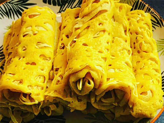 Three rolled net crepes from "A Taste of Indonesia" by Event, featuring a yellow lacy pattern, are arranged on a decorative plate—ideal for an Asian-themed gathering or to elevate your next meal. Leaf designs accent the background.