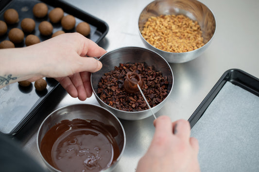 At the Event Chocolate Experience, a pastry chef coats truffles in melted chocolate and cocoa nibs, surrounded by trays of treats and bowls of toppings—capturing the artistry of chocolate making.