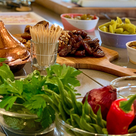 Experience the French Bistro by Event: a wooden board with dates, walnuts, and grapes, surrounded by pickles, fresh herbs, red onion, and red bell pepper—ideal for exploring classic French dishes in a fun cooking class.