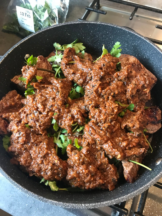 A Taste of Indonesia by Event is showcased in a pan with cooked meat topped in reddish-brown sauce and fresh green herbs, capturing authentic Indonesian flavors. A coriander packet appears in the background.