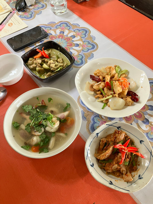 South East Asia on a Plate by Event features four beautifully arranged Thai and Indonesian dishes: green curry, spicy meat with red chilies, stir-fried vegetables, and herbal soup, highlighting the vibrant flavors of Southeast Asia.