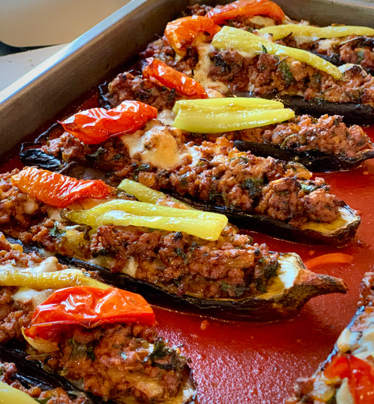 Eastern Mediterranean Feast by Event features stuffed eggplants with savory ground meat, topped with peppers, baked in tomato sauce, and arranged in a metal tray—a delicious dish inspired by authentic Turkish cuisine.