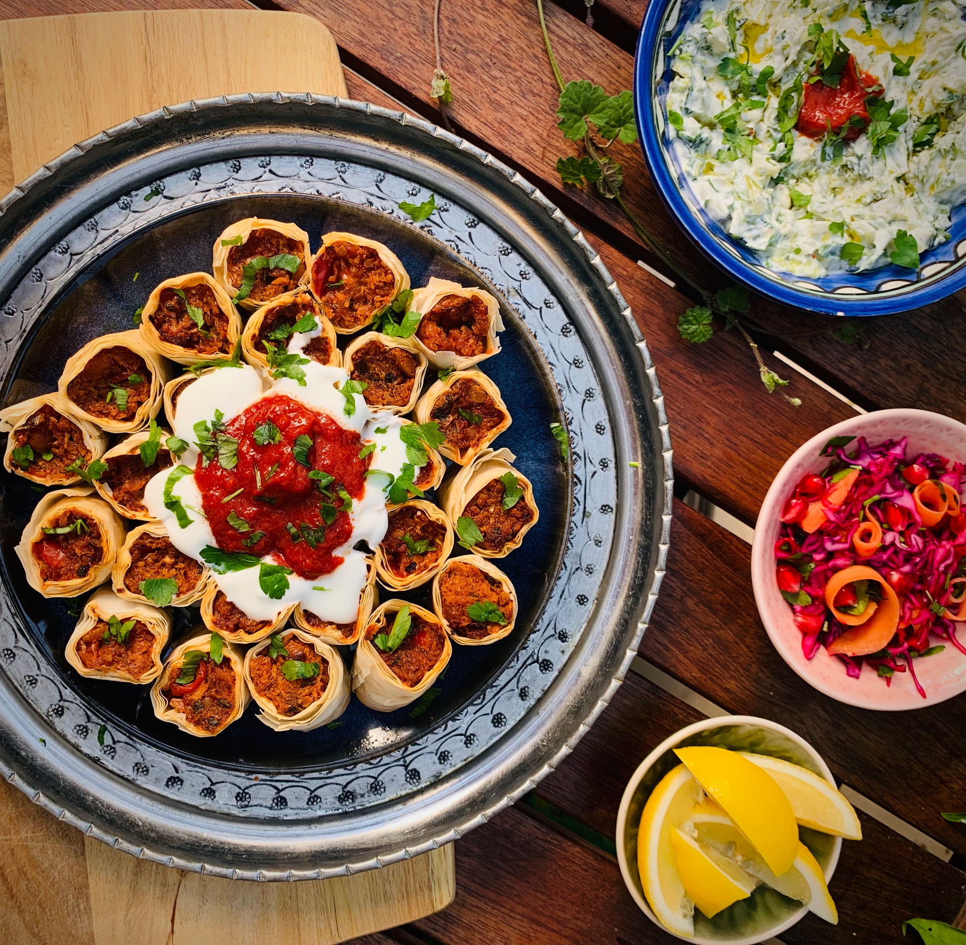 Experience bold vegetarian flavours with Event’s Mastering Bold Vegetarian Flavours—a tray of rolled pastries topped with yogurt and red sauce, served with tzatziki, red cabbage salad, and lemon wedges for an authentic Turkish feast.