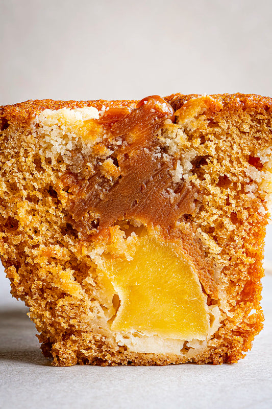 Close-up of Honesty’s Apple & Caramel Muffin, sliced to display its golden-brown crumb with rich caramel swirls and a piece of apple inside, set against a softly lit, plain background.