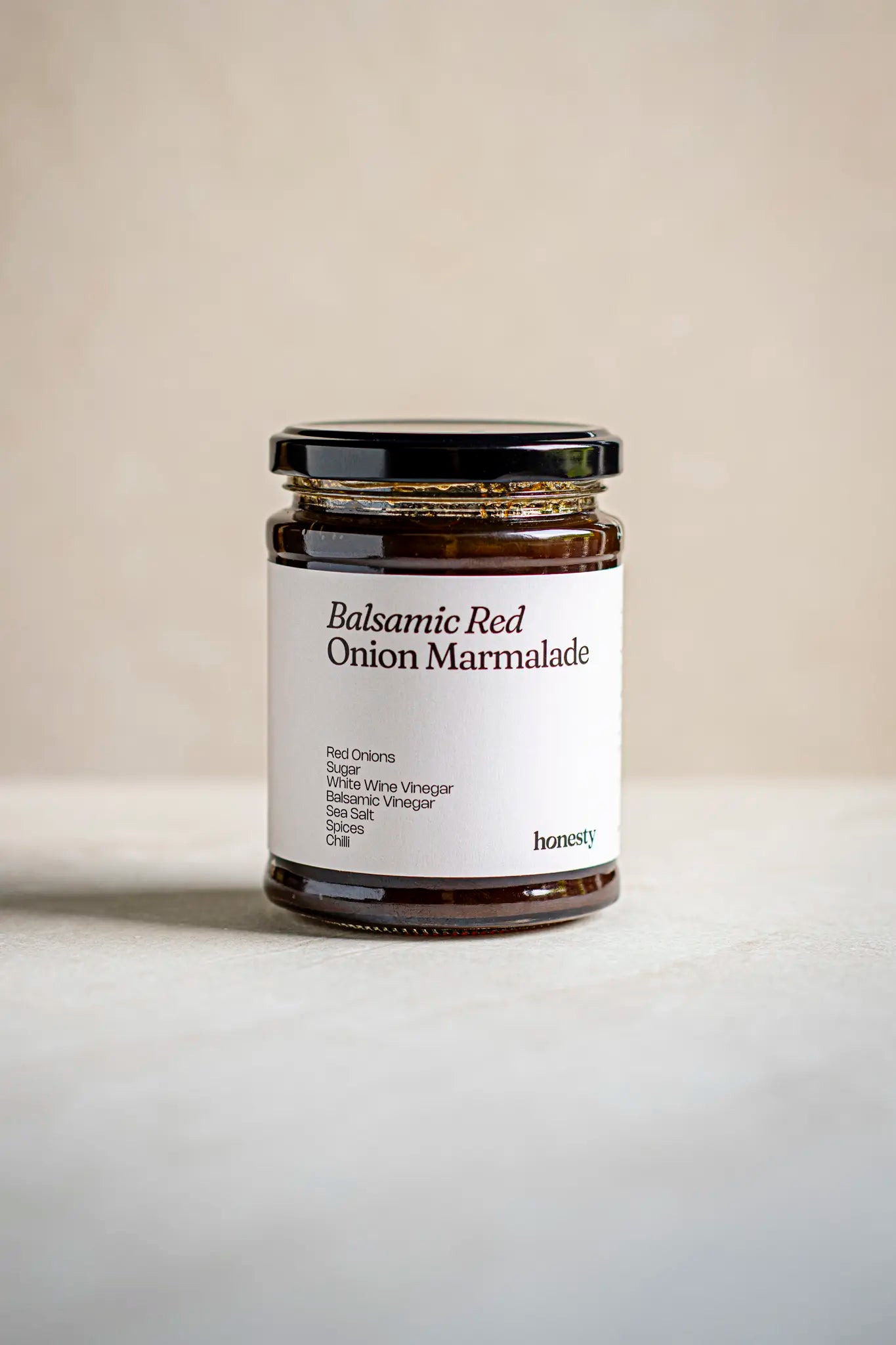 A glass jar of Honesty Balsamic Red Onion Marmalade with a black lid and white label, containing red onions, sugar, white wine vinegar, balsamic vinegar, sea salt, and spices.