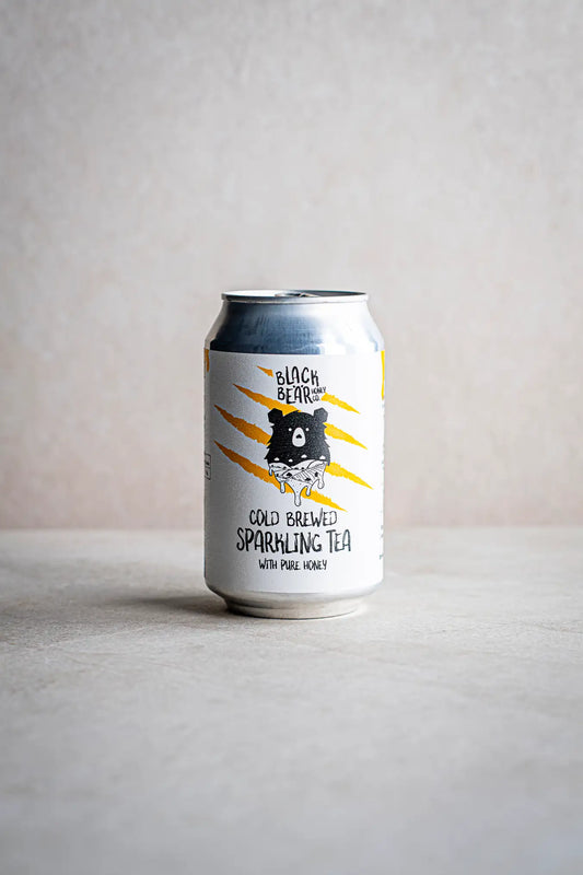 A can of Honesty Cold Brewed Sparkling Tea with Pure Honey rests on a light surface against a neutral background, its label displaying an illustrated bear and bold yellow claw marks.