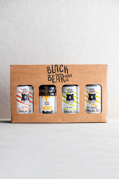 The Honesty Black Bear Honey Co. Gift Pack includes three cans of Cold Brewed Sparkling Tea and a jar of pure honey, each with a bear logo and colorful stripes, presented against a plain background.