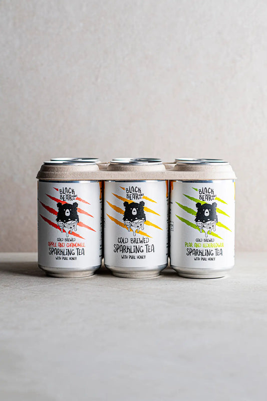 Three cans of Honesty Cold Brewed Sparkling Tea with Pure Honey—apple & chamomile, classic, and elderberry—are side by side on a neutral background. Each can displays a black bear illustration with vibrant claw marks.