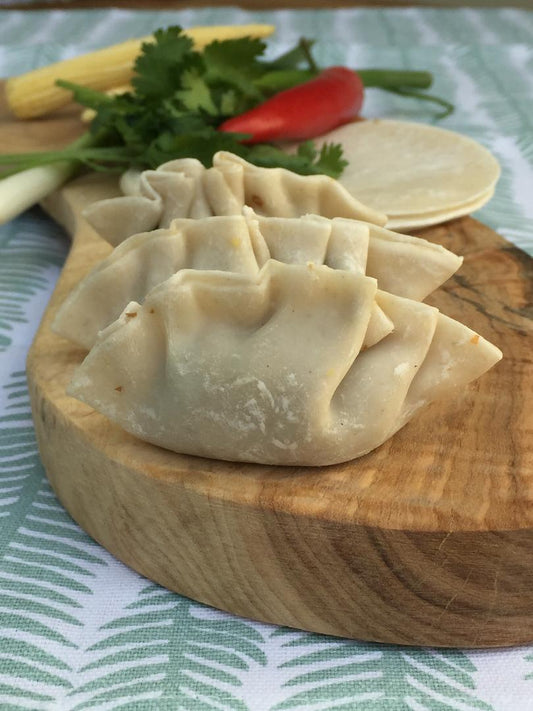 Three uncooked dumplings rest on a wooden board surrounded by vibrant veggies—perfect inspiration for your next traditional meal or to enjoy at the Chinese Cookery Class by Event.