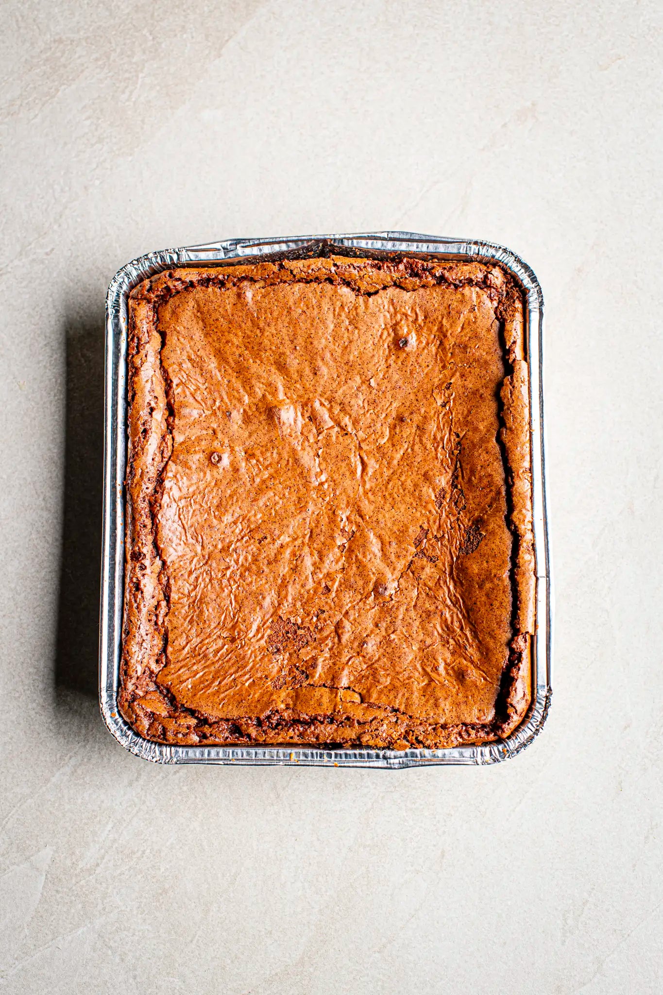 A handmade rectangular Honesty chocolate brownie, baked in a disposable aluminum foil tray, sits on a light-colored countertop.