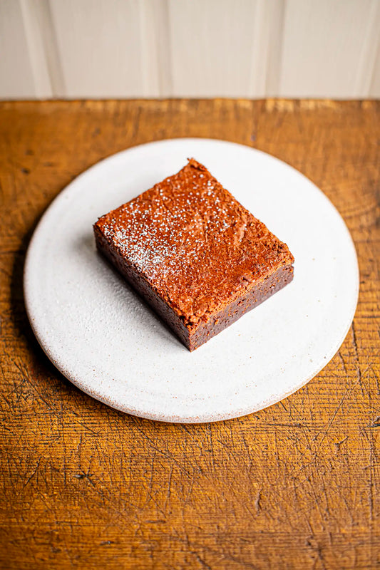 A single Honesty chocolate brownie sits on a round white plate, placed on a wooden surface.