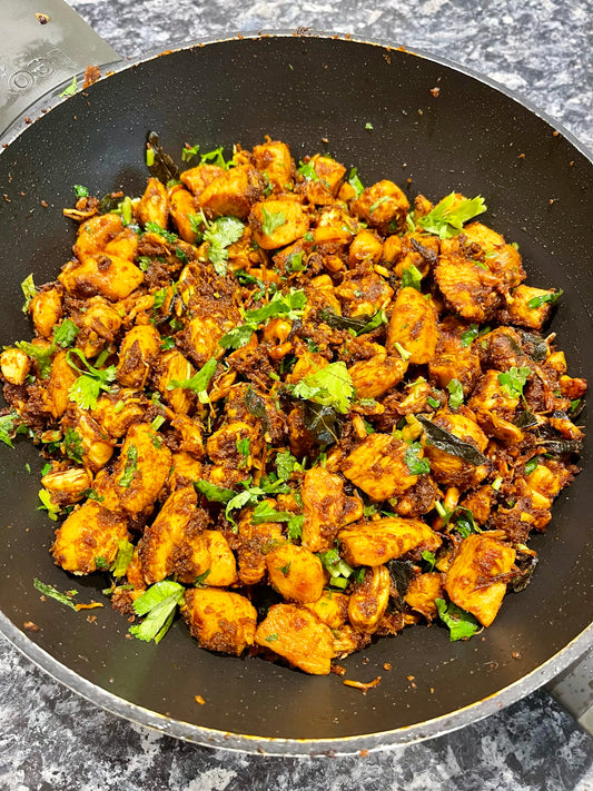 A pan of spiced chicken garnished with cilantro sits on a gray granite countertop—showcasing South Indian flavors from the Event One Pot Masterclass.