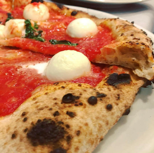 Close-up of a Neapolitan-style veggie pizza with charred crust, mozzarella, and basil. Get inspired for your next fun session with the Childrens Pizza Making Course by Event!.