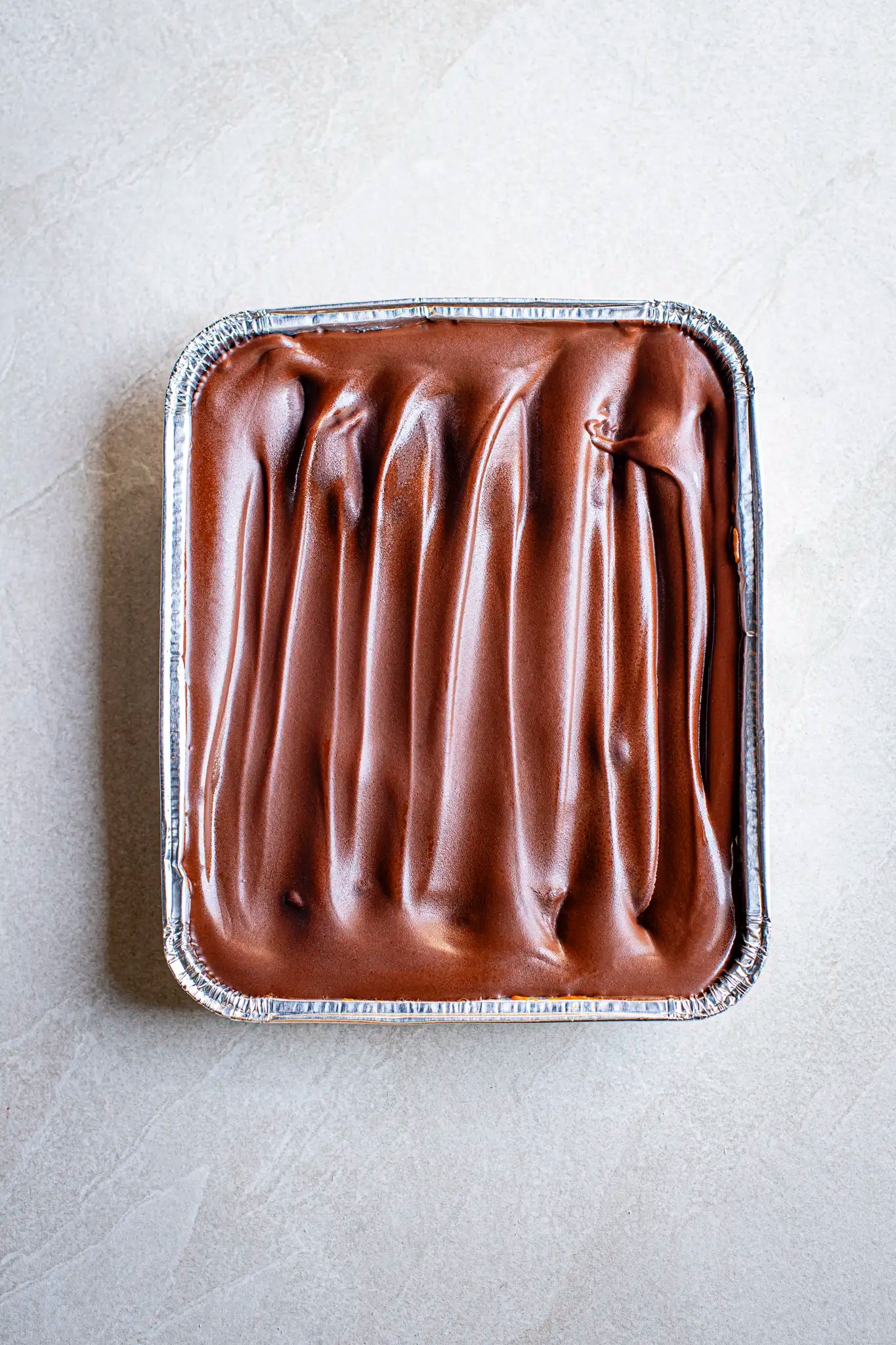 A rectangular foil tray holds Honestys Millionaires Shortbread topped with smooth, glossy chocolate frosting and elegant swirls—ideal for handmade dessert lovers.