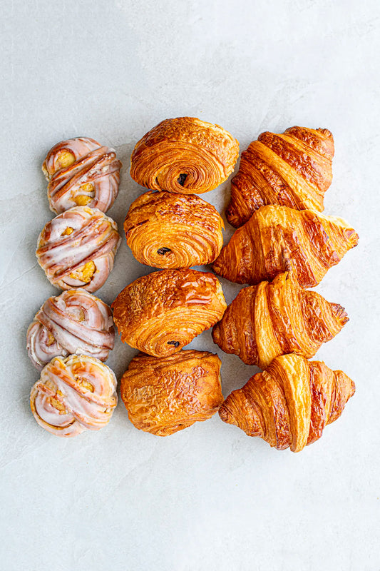 An overhead view of Honesty’s The Morning Brief pastries arranged in rows on a light surface, featuring swirl buns with icing, Madagascan Vanilla Bun, Pain au Chocolat, and golden brown Plain Croissant.