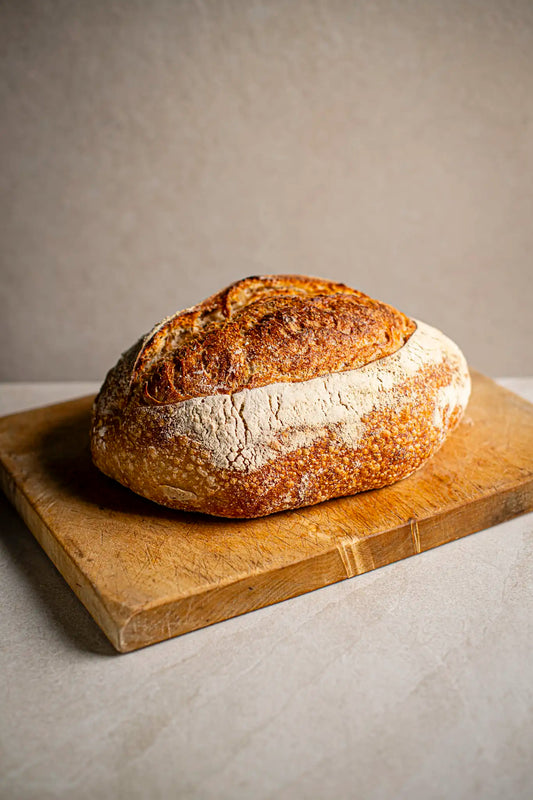 A classic Sourdough by Honesty sits on a wooden cutting board against a plain, light background, highlighting the charm of authentic, handmade treats.