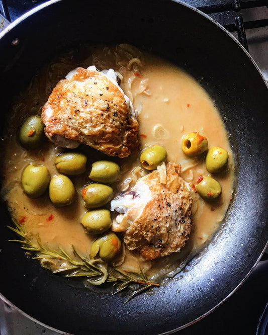 Event Spanish Tapas features chicken thighs with golden skin simmered in a creamy sauce with green olives, onions, and rosemary—perfect for serving right from the black skillet on your stovetop.