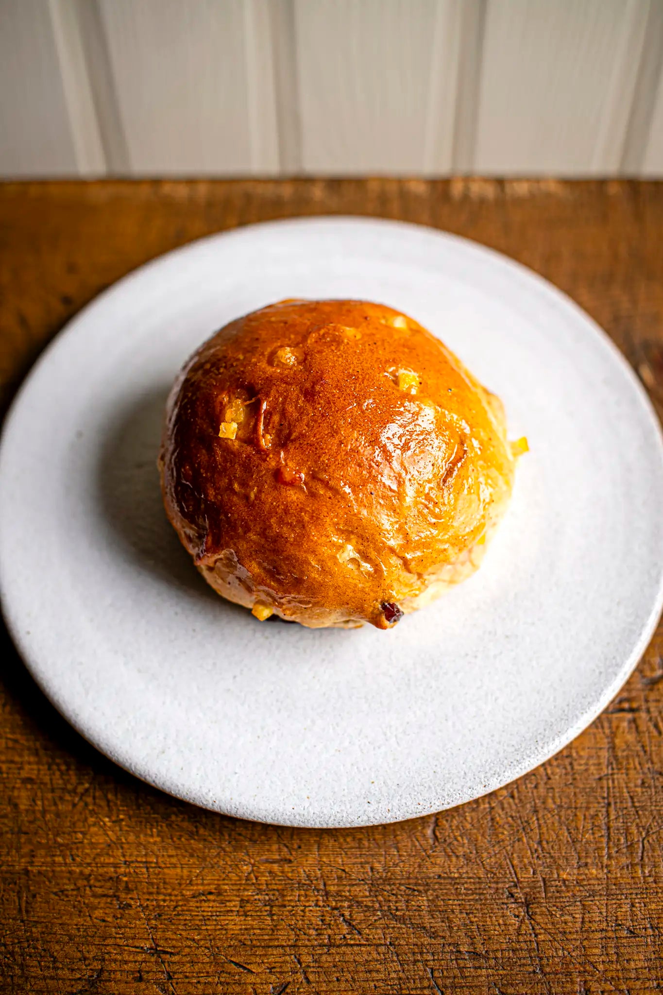 A slice of Honesty’s Victoria Sponge, golden-brown with a shiny top and visible chunks inside, sits freshly baked on a white plate atop a wooden surface.