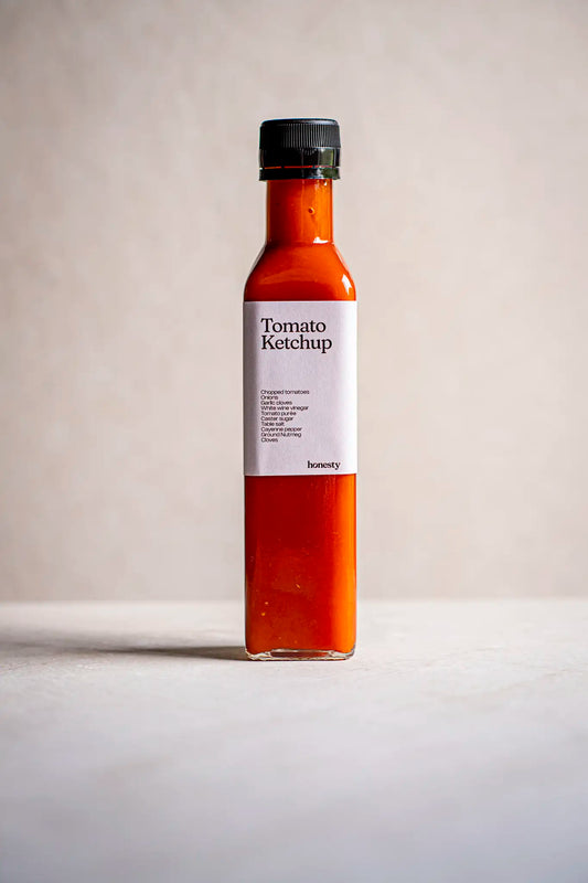 A clear glass bottle filled with Victoria Sponge sauce by Honesty, featuring a black cap and a white label reading Victoria Sponge. This handmade product is displayed on a light surface with a plain background.